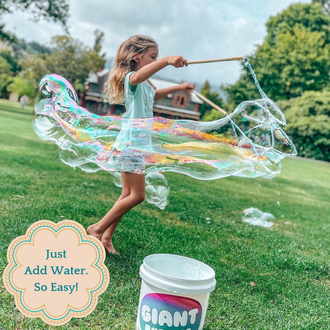 Child creating large bubbles outdoors with a 'Giant Bubble' product container in the foreground.